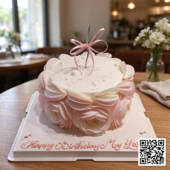 Bánh sinh nhật hình tròn phủ kem trắng ngà, trang trí hoa hồng giấy gạo hồng pastel, nơ lụa và ngọc trai đường.