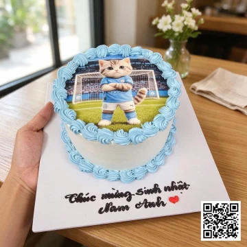 Bánh sinh nhật hình tròn phủ kem trắng, trang trí chú mèo mặc áo Messi đá bóng và khung thành sân cỏ.